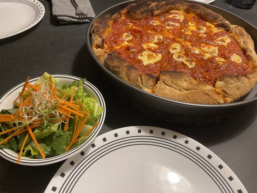 A deep dish pizza, a salad, and an empty plate ready for dinner. 