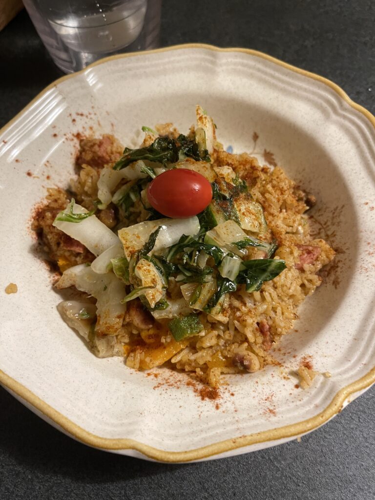 Smoky Rice and beans with sautéed greens and a bright red cherry tomato on top in a stoneware bowl 