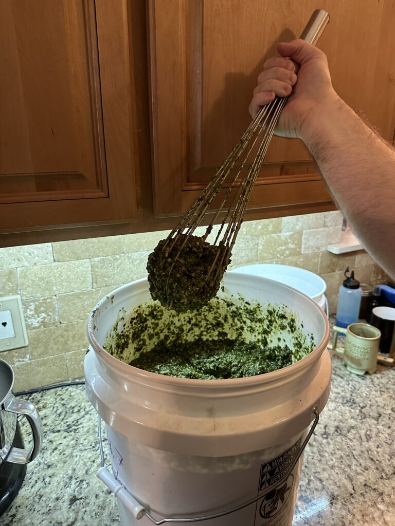 The Chef wields a pesto-laden giant whisk above the food safe five gallon bucket. 