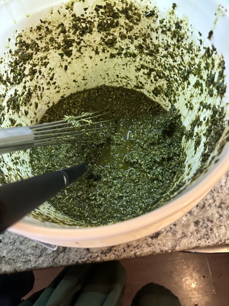 A view into the now half empty big bucket of pesto with the ladle and whisk