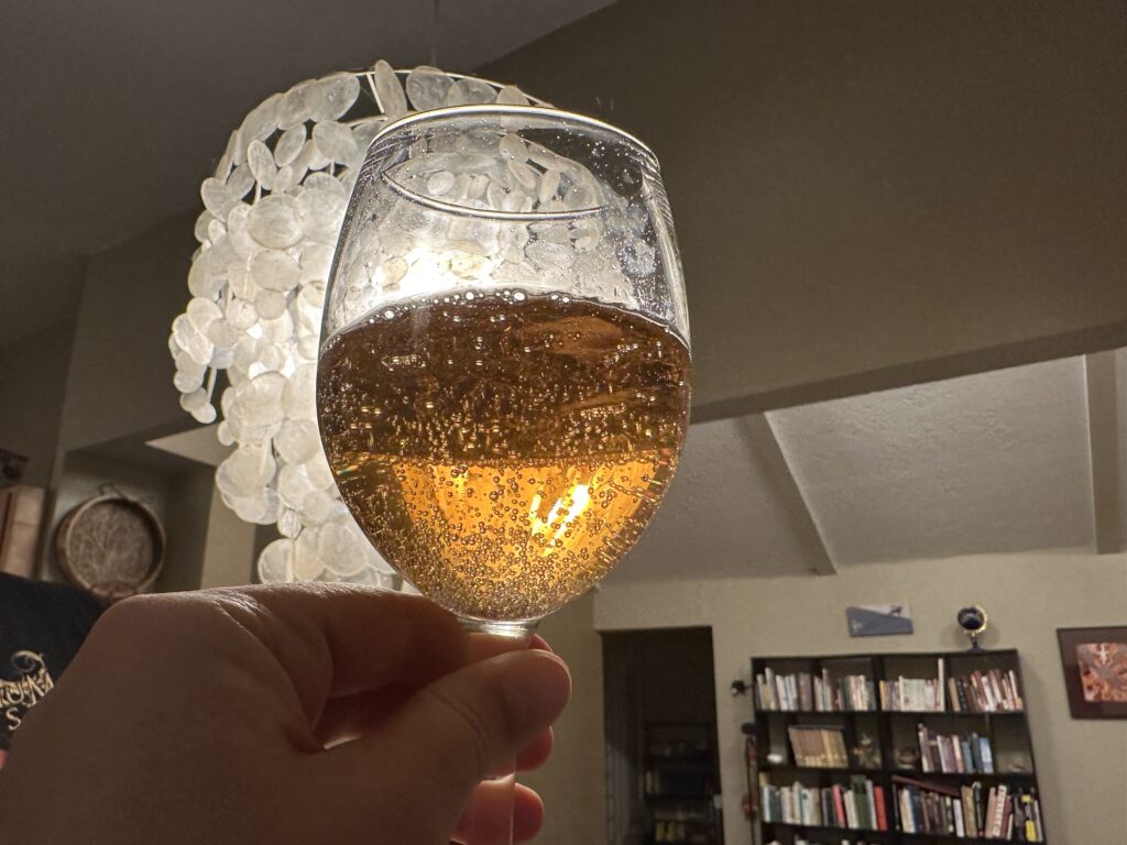 I’m holding a wineglass of sparkling beverage up to the 1970s shell chandelier that came with the house.  The backlighting shows off the abundant bubbles in the bubbly. 